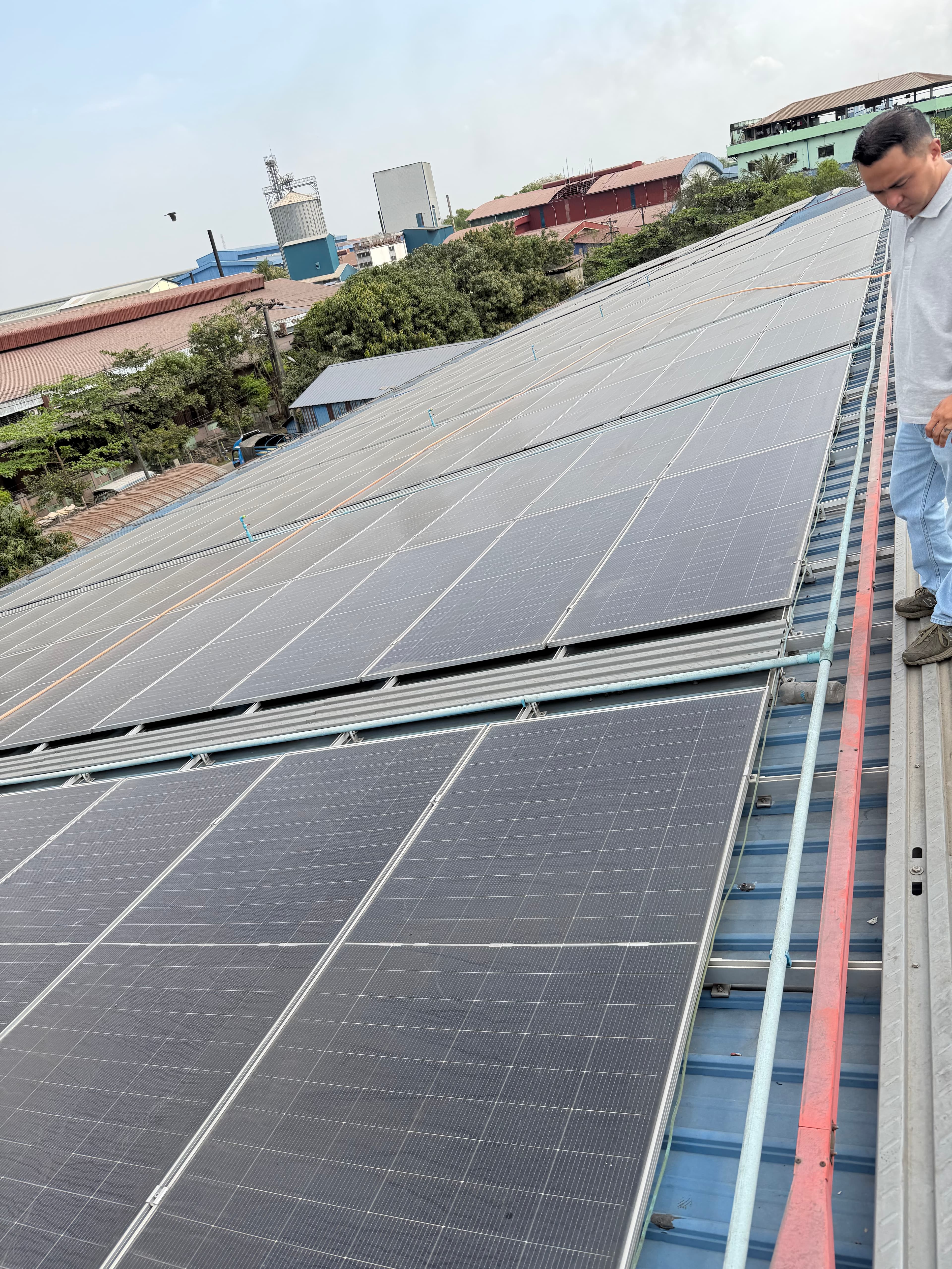 Man standing on a rooftop beside a large array of solar panels overlooking a city.