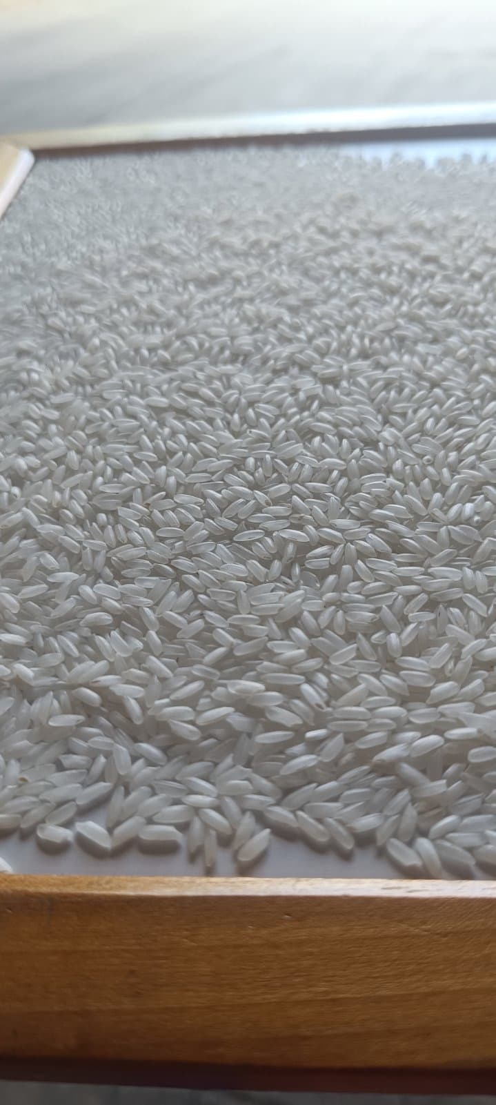 Close-up of white rice grains spread out on a flat surface with wooden trim.